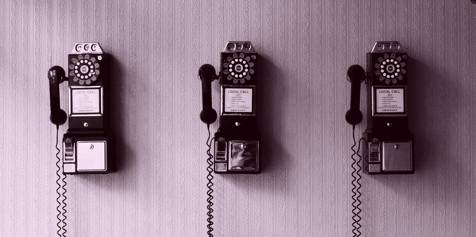 Three, old telephones, lined up on a wall. The picture is in black and white.